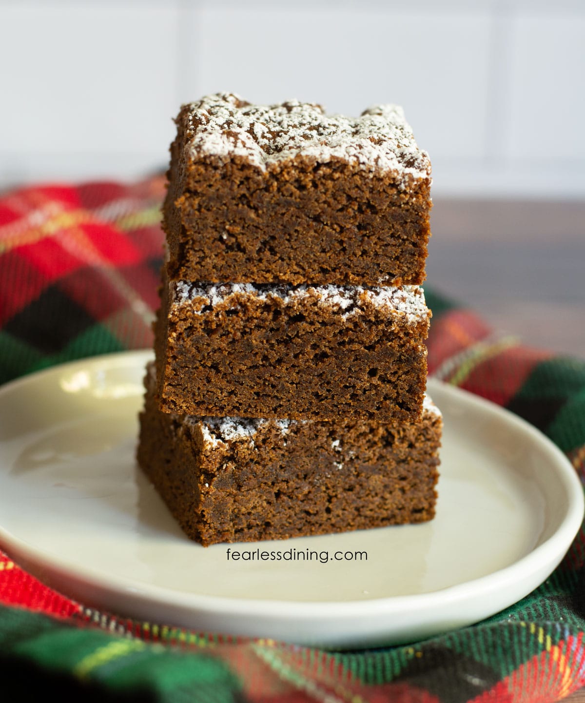 A stack of three gluten free gingerbread cookie bars on a small white plate.