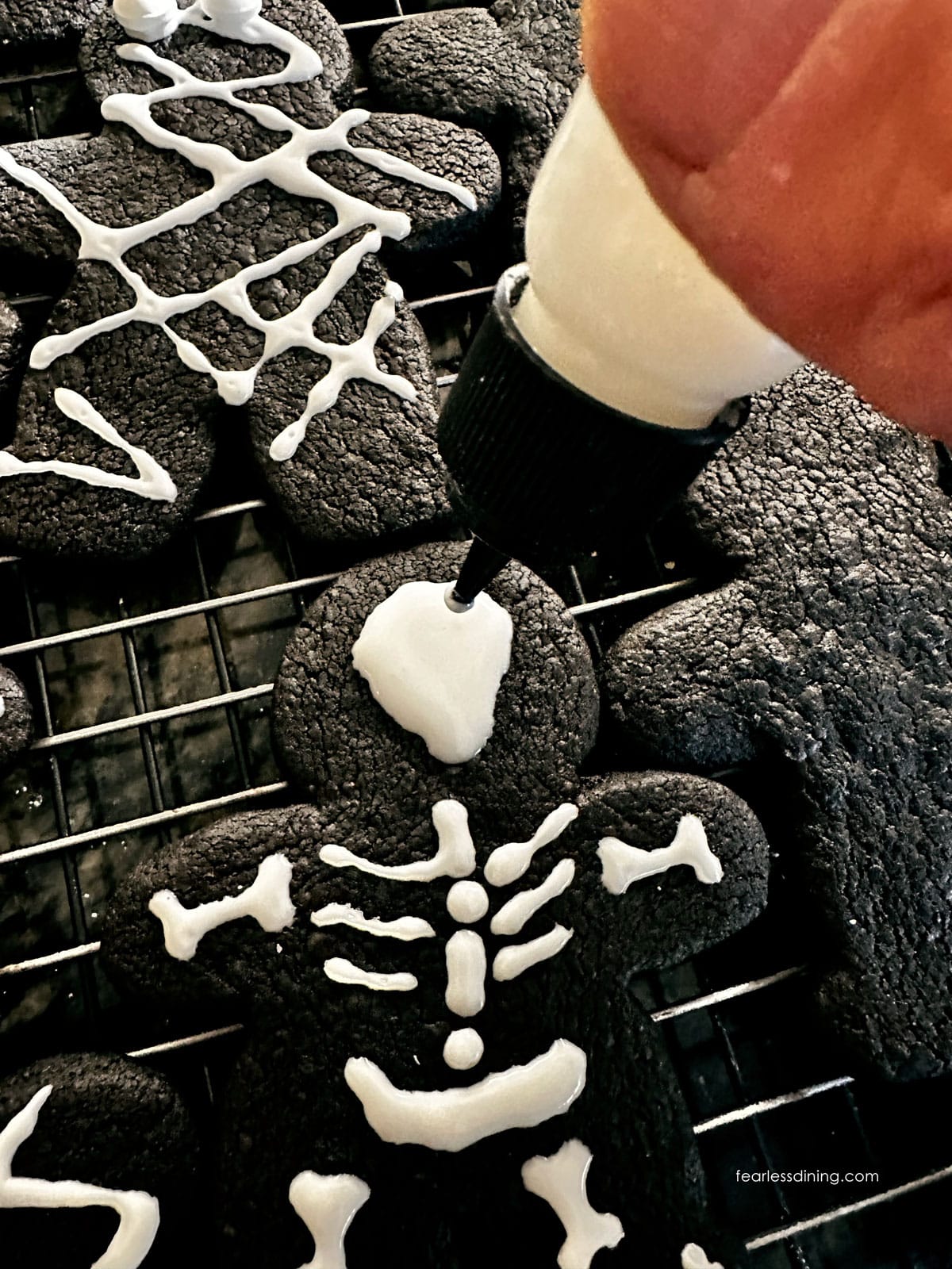Using a small squeeze bottle with royal icing to make a skeleton pattern on the cookies.