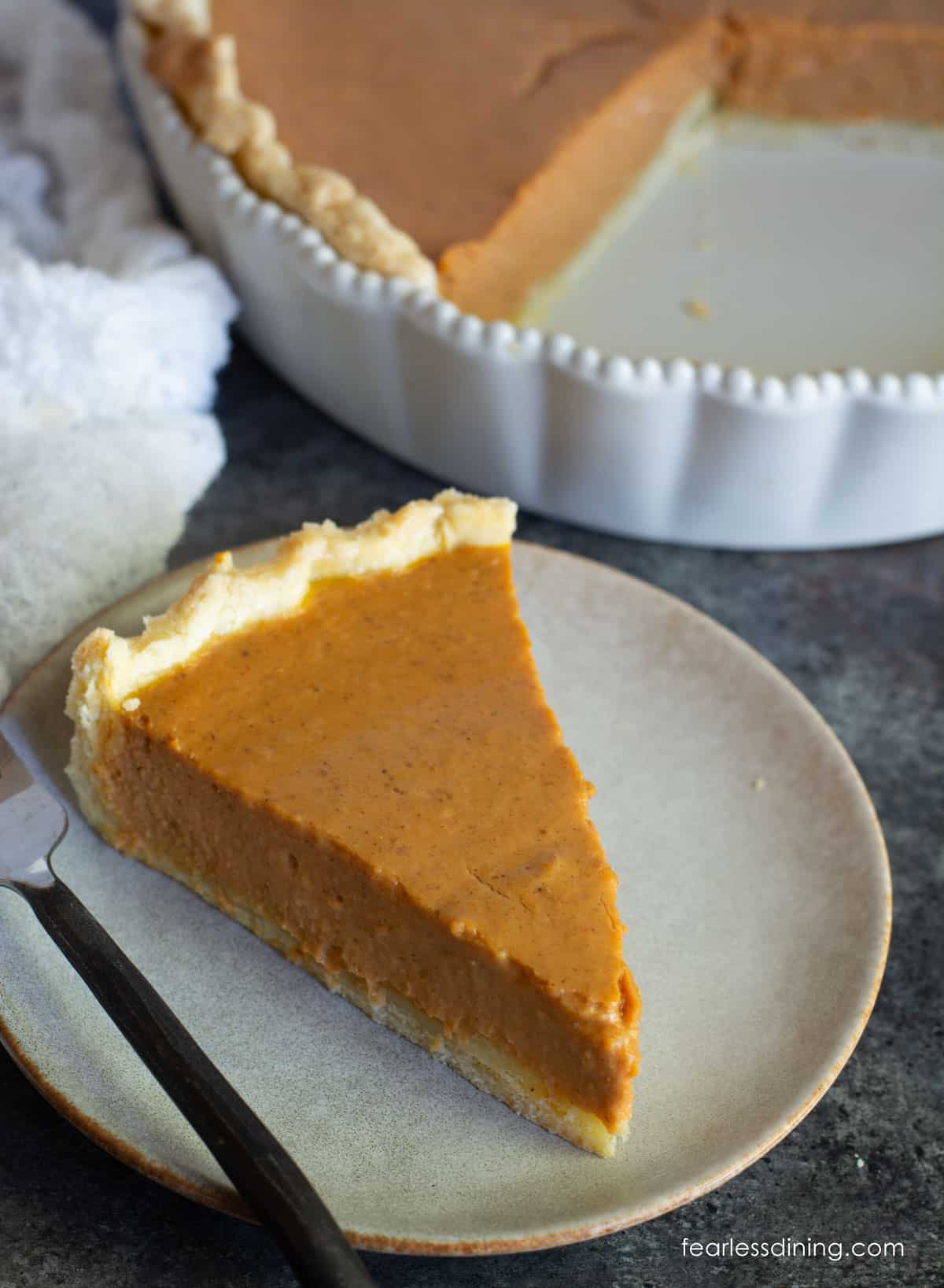 A slice of gluten free pumpkin pie on a plate next to a whole pie.