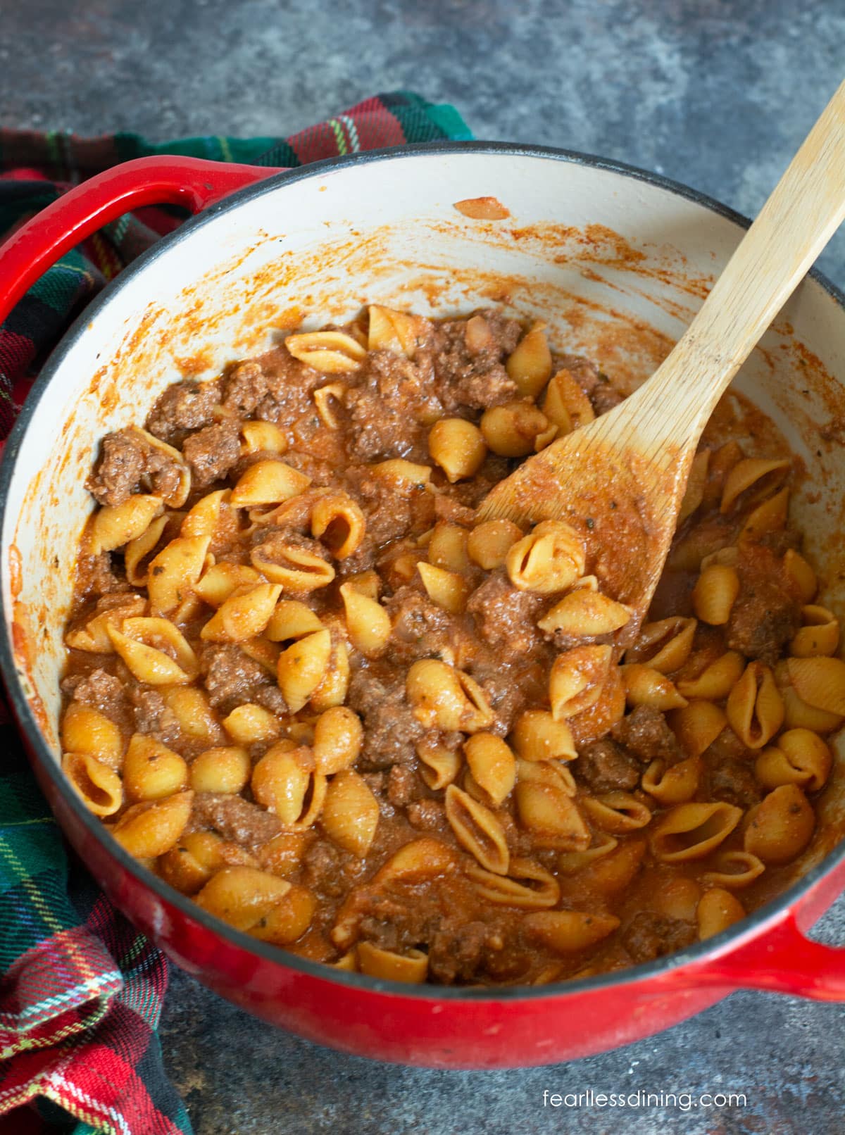 A red Dutch oven pot filled with the cooked beef and shell pasta.