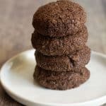 A stack of four gluten free chocolate snickerdoodle cookies on a white plate.