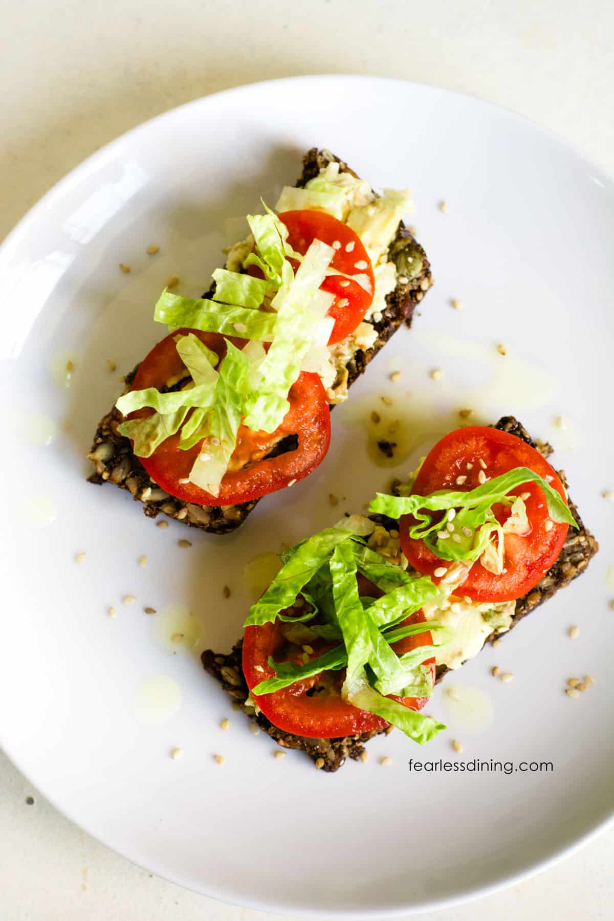Two slices of seed bread topped with avocado, sliced tomato and shredded lettuce.