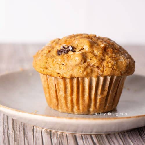 A single gluten-free carrot muffin on a plate. It has a large bakery style dome top.