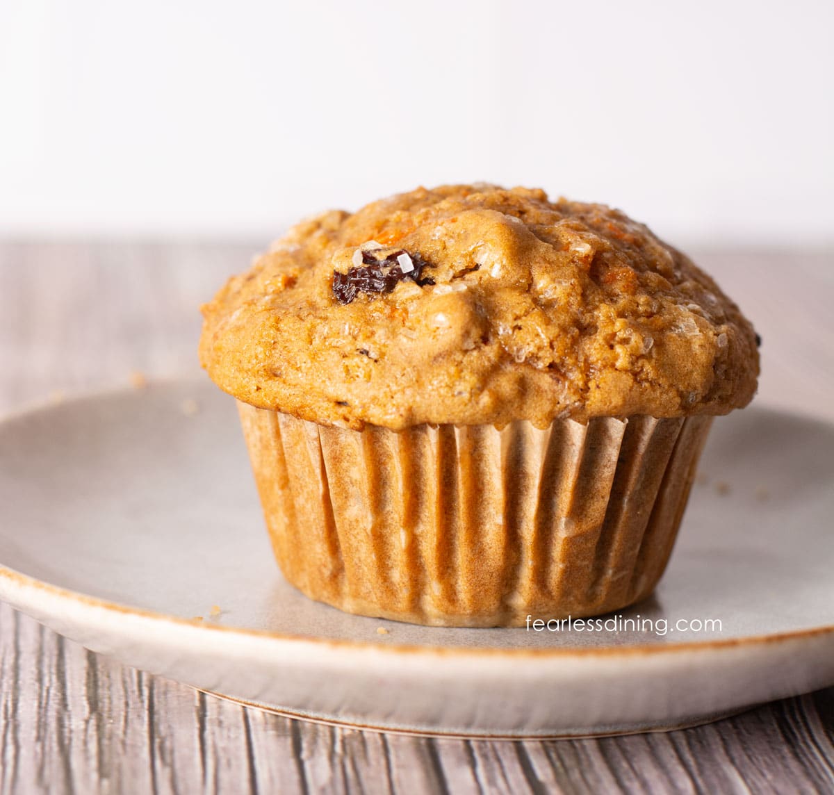 A single gluten-free carrot muffin on a plate. It has a large bakery style dome top.