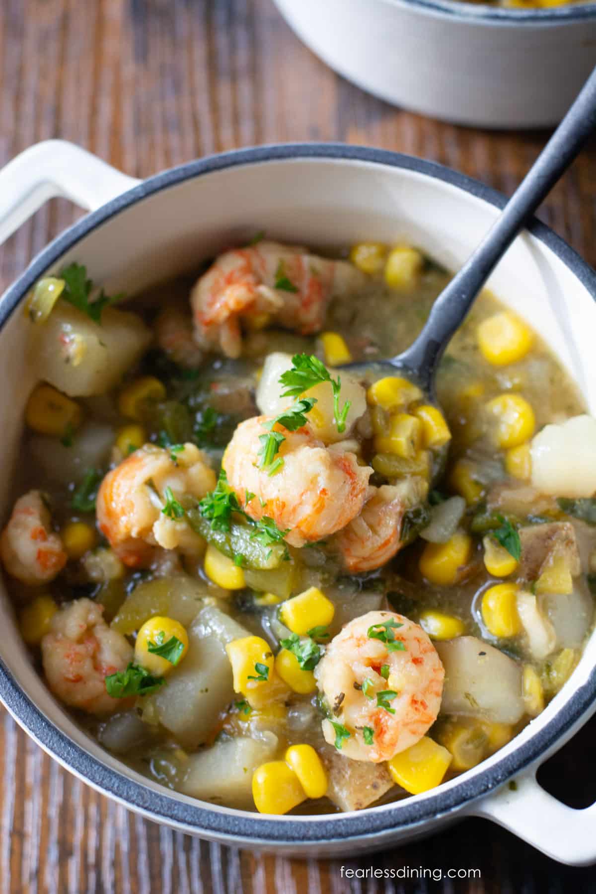 A close up of a bowl of corn and crawfish soup on a wooden table.