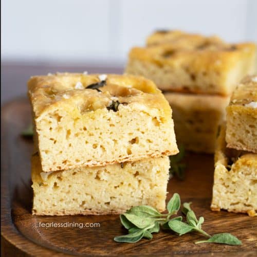 Square pieces of gluten free sourdough discard focaccia bread on a wooden cutting board.