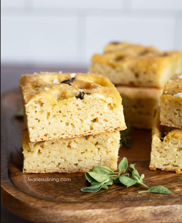 Square pieces of gluten free sourdough discard focaccia bread on a wooden cutting board.