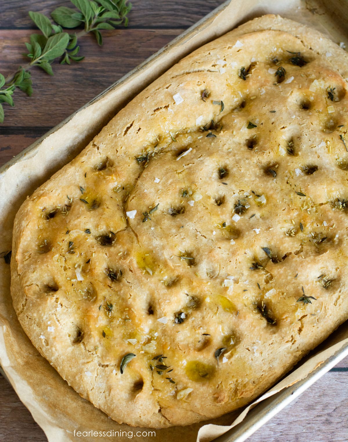 Baked gluten free focaccia on a baking pan with olive oil drizzled over the top.