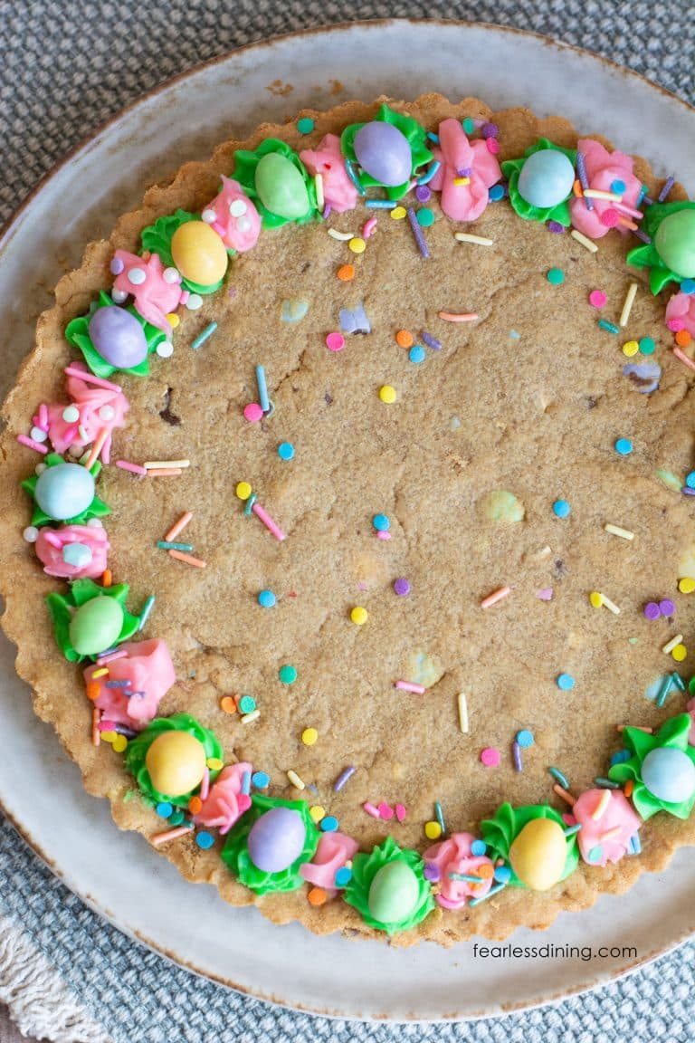 The top view of a gluten free peanut butter cookie cake. It is loaded with M and Ms and decorated with pastel frosting and sprinkles.