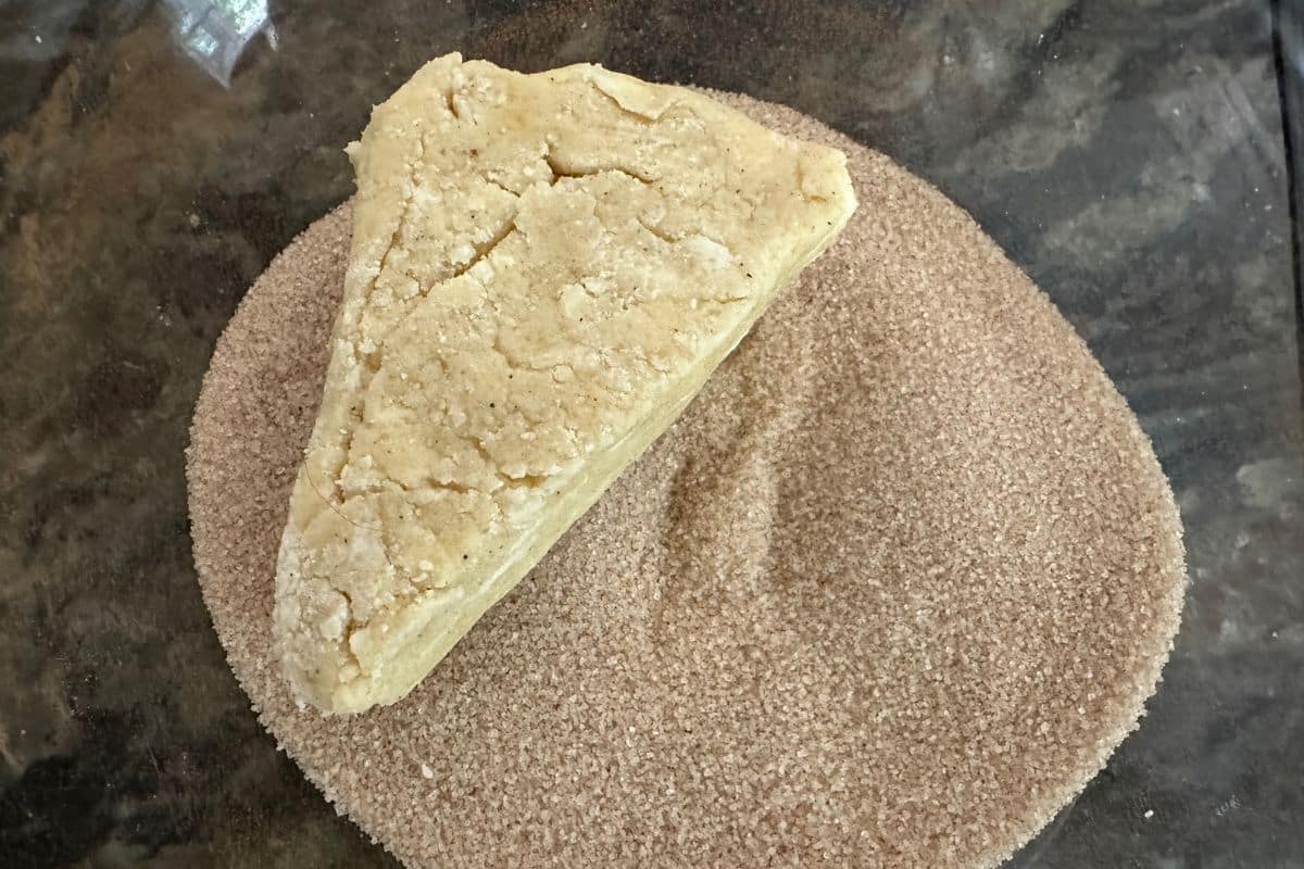 A scone wedge of dough in the cinnamon sugar mixture.