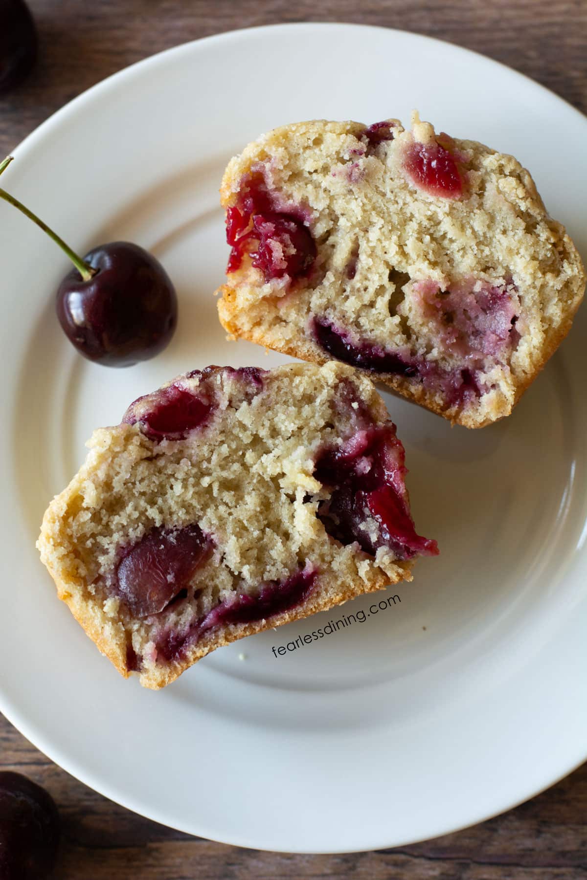 A cherry muffin cut in half on a plate soyou can see how fluffy they are.