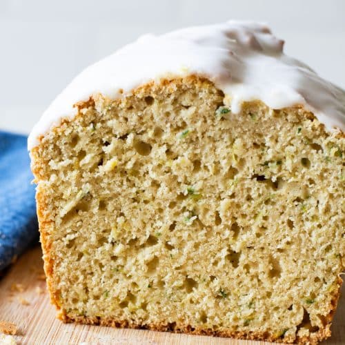 A loaf of gluten-free lemon zucchini bread sliced on a cutting board so you can see the inside.