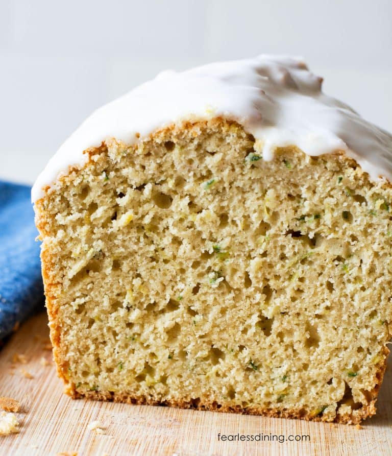 A loaf of gluten-free lemon zucchini bread sliced on a cutting board so you can see the inside.