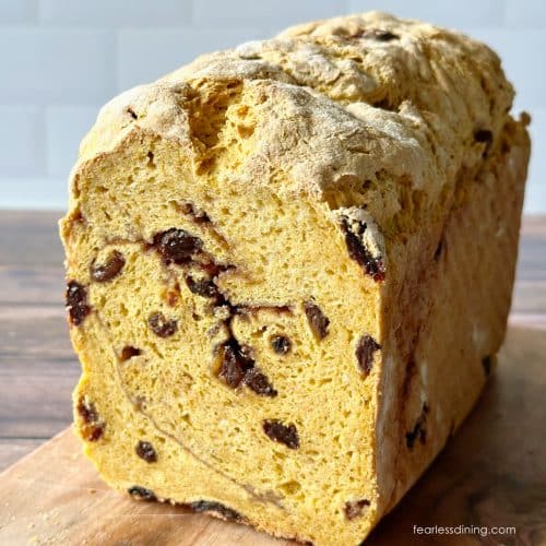 The front of a loaf of a yeasted gluten-free pumpkin raisin bread on a wooden cutting board.