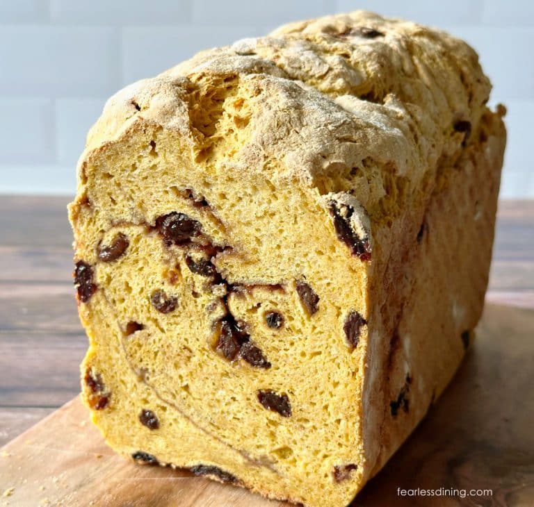 The front of a loaf of a yeasted gluten-free pumpkin raisin bread on a wooden cutting board.