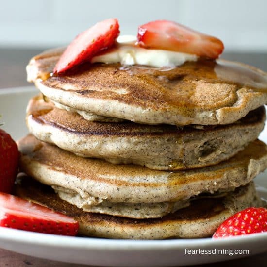 A stack of four gluten free buckwheat pancakes with strawberries and maple syrup.