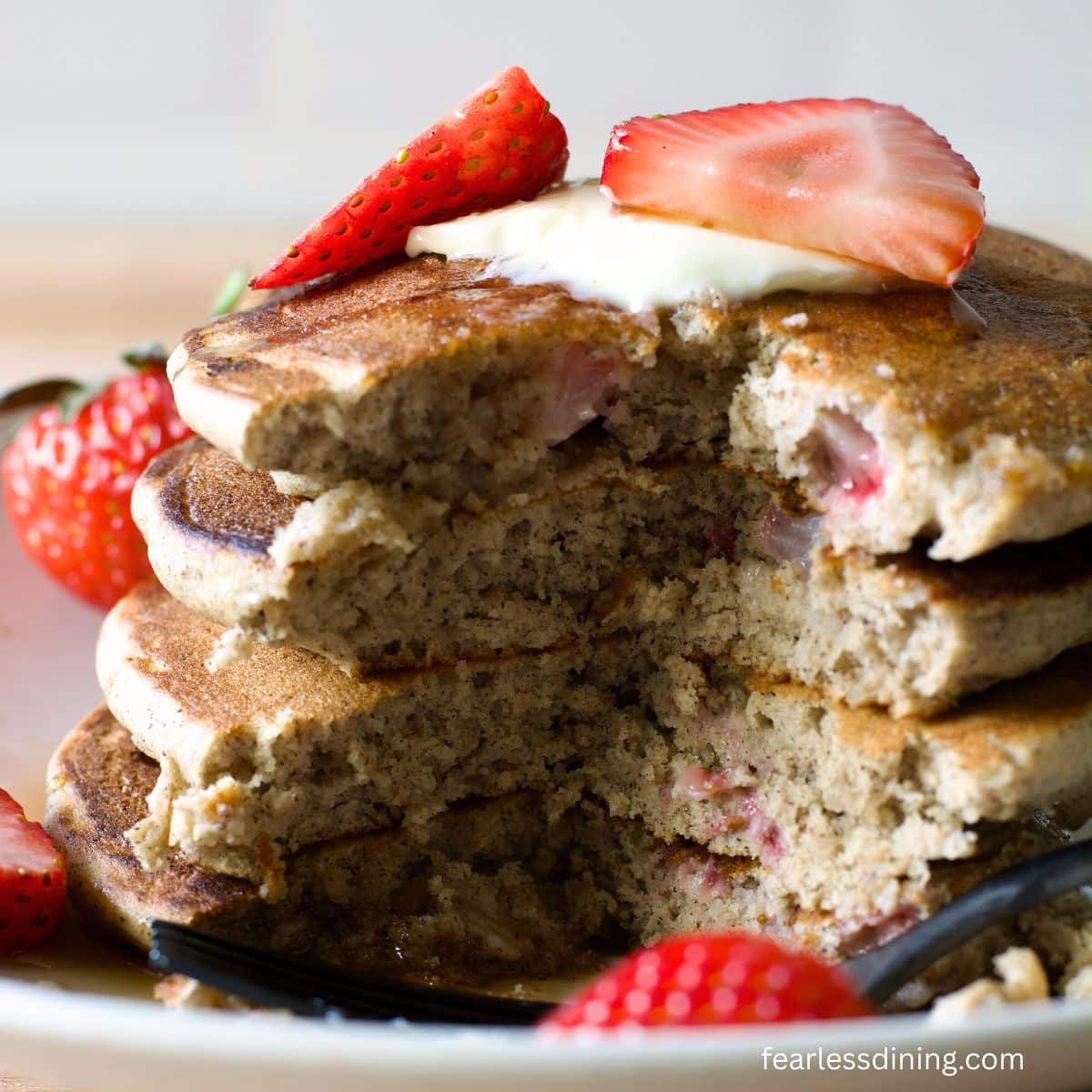 A stack of strawberry buckwheat pancakes with a portion cut out so you can see the fluffy interior.