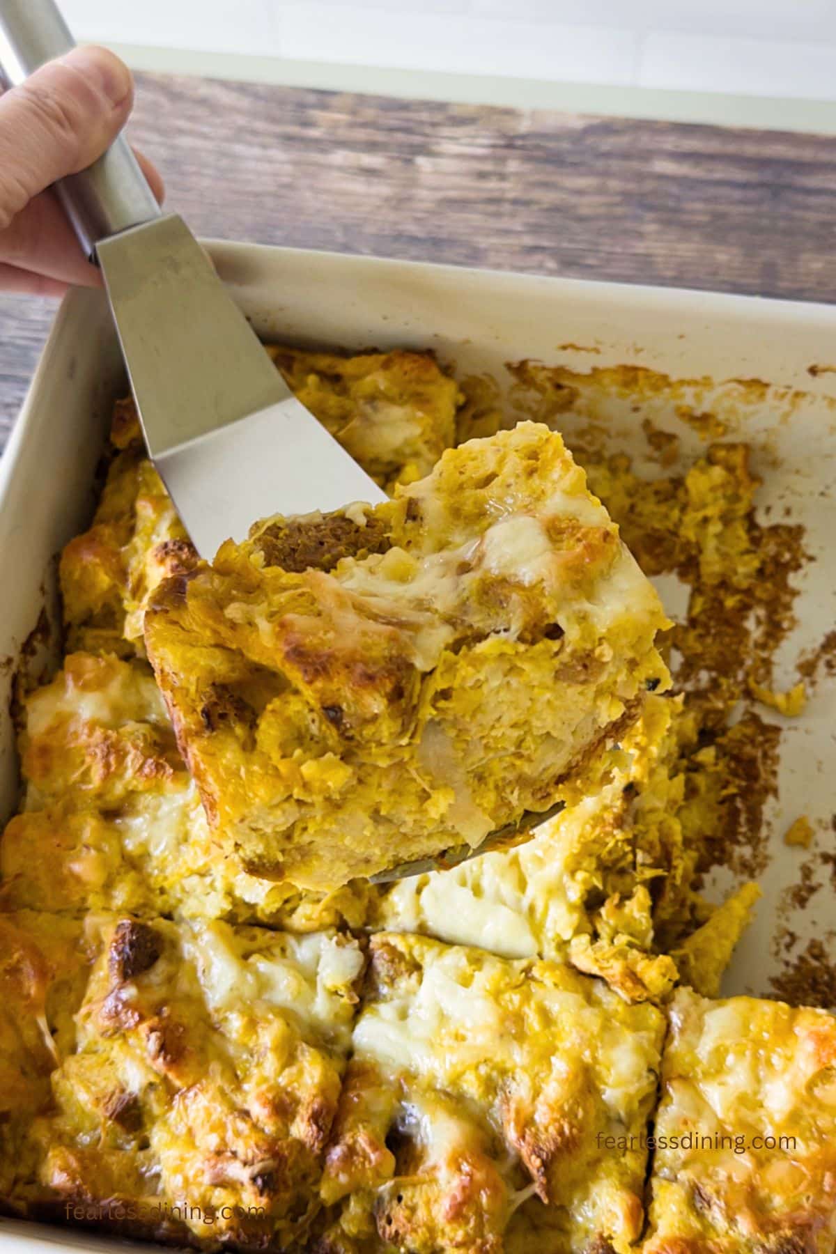 A spatula holding up a slice of the savory gluten-free pumpkin onion bread pudding.
