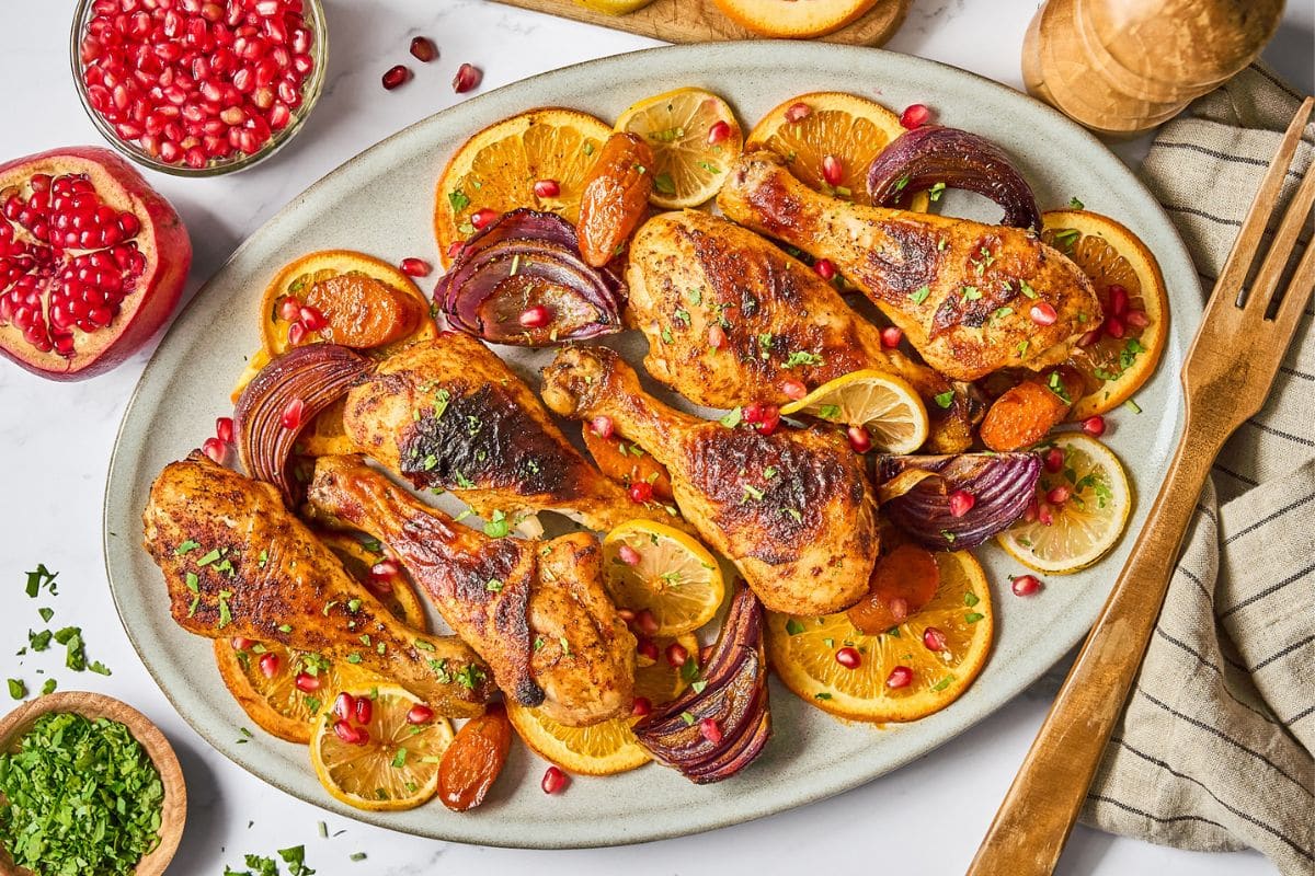 A serving platter with the chicken drumsticks, onions, and oranges.