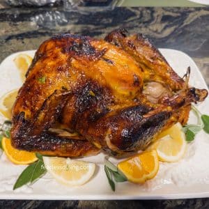 A roasted turkey with orange marmalade and sage on a platter with sliced oranges and lemons.