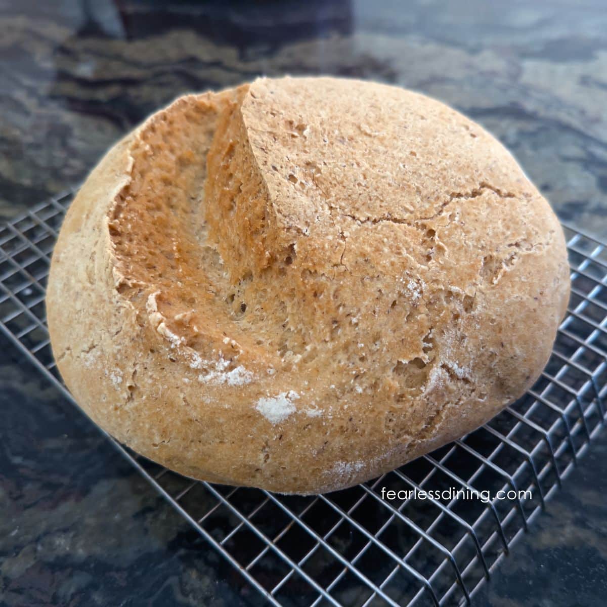 A round gluten free artisan bread boule on a cooling rack.