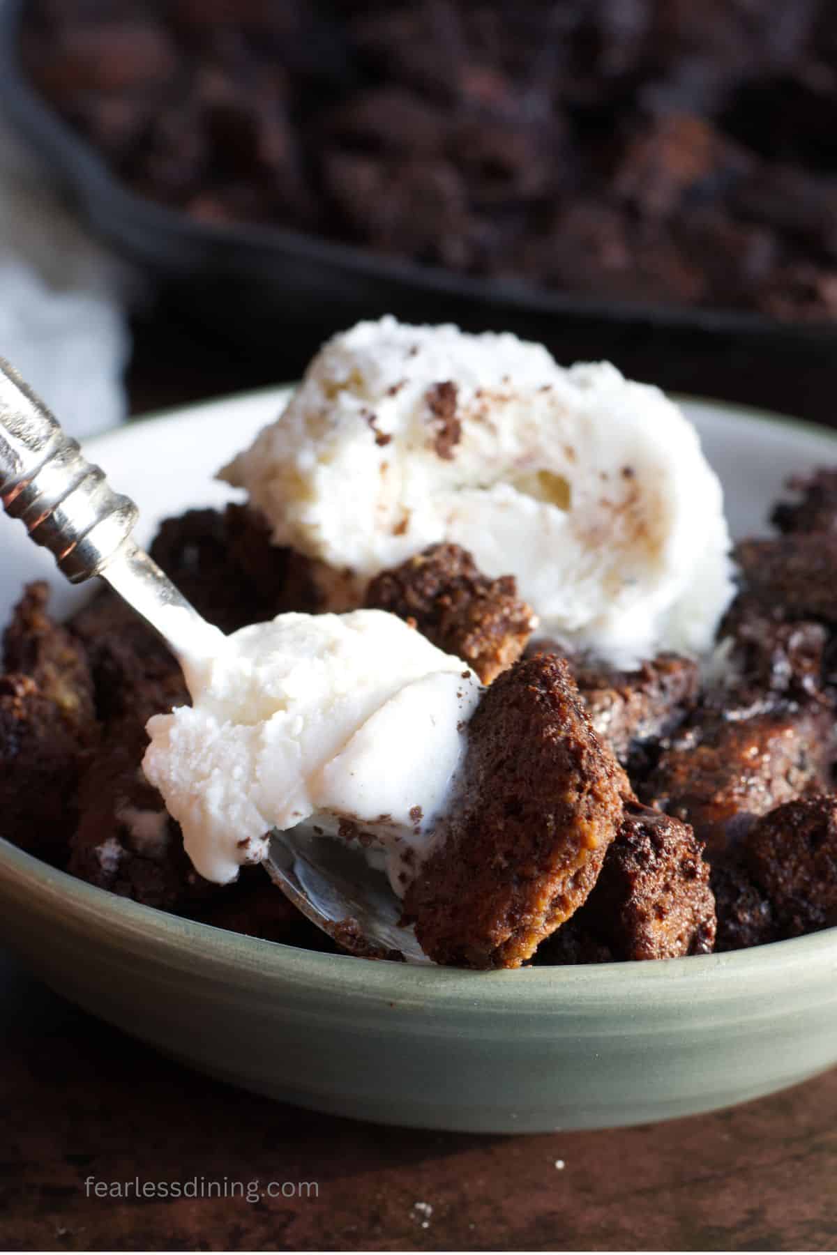 A spoon with a bite of ice cream and gluten free chocolate bread pudding.