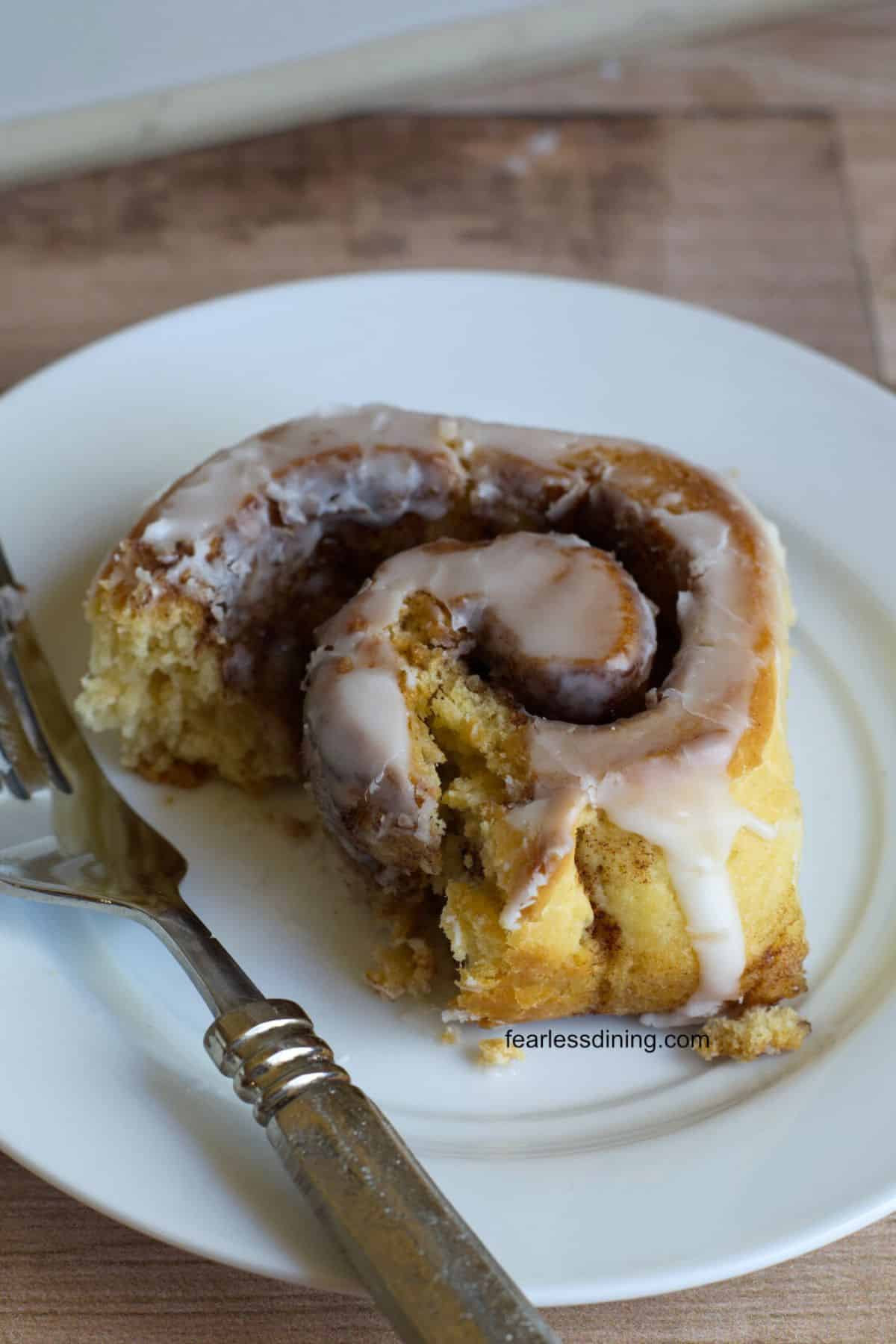 A gf sourdough cinnamon roll with a bite taken out on a plate.
