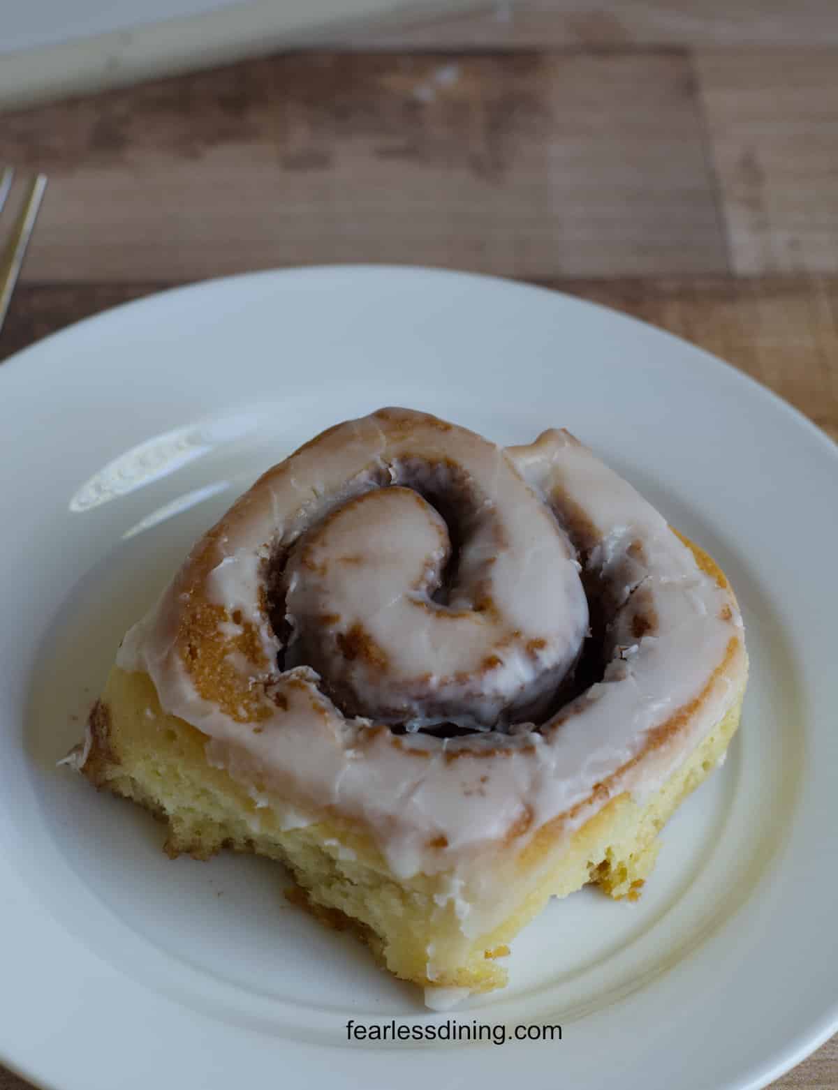 An iced gluten free sourdough cinnamon roll on a small white plate.