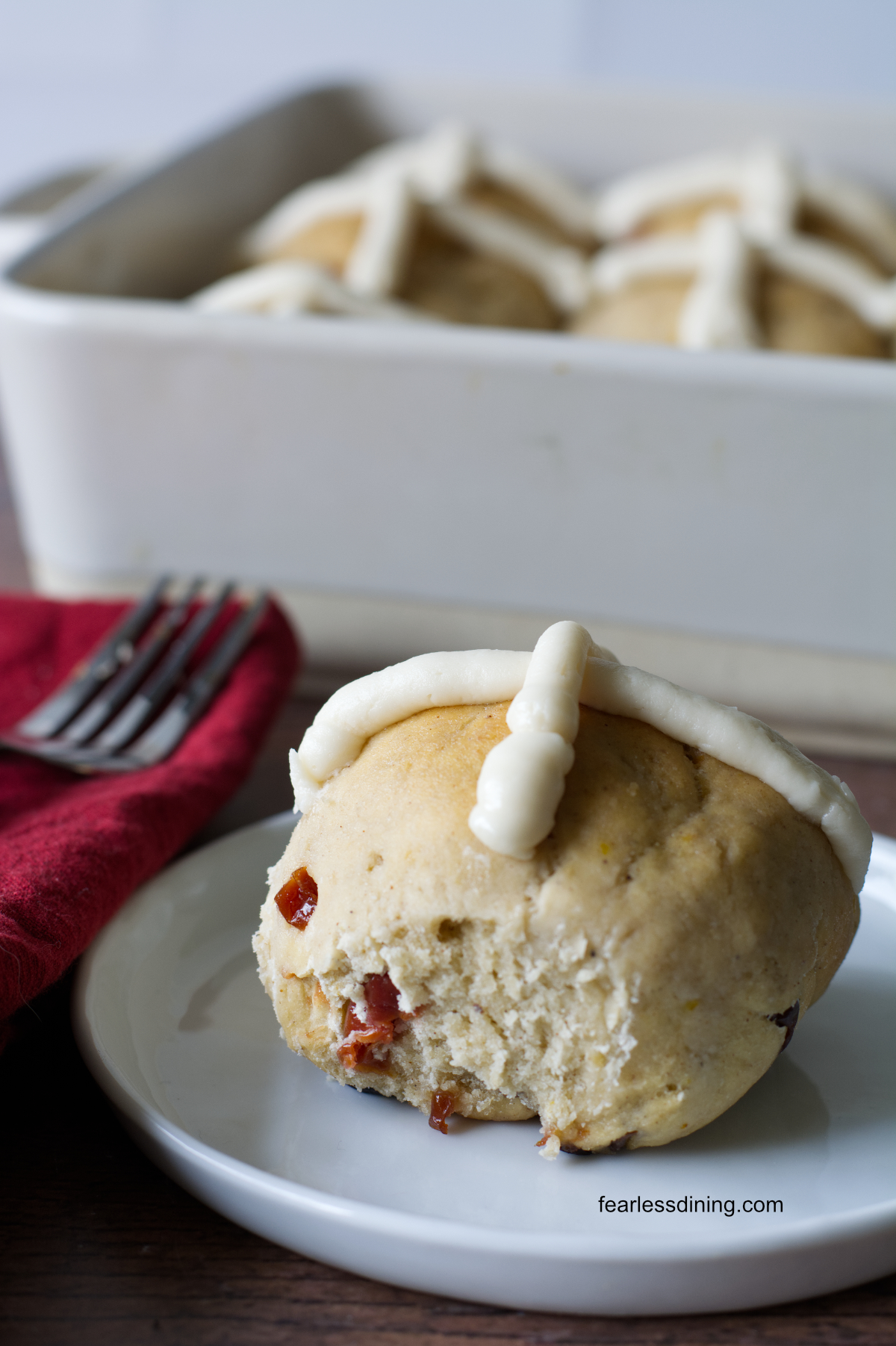 A gluten free hot cross bun on a small white plate.