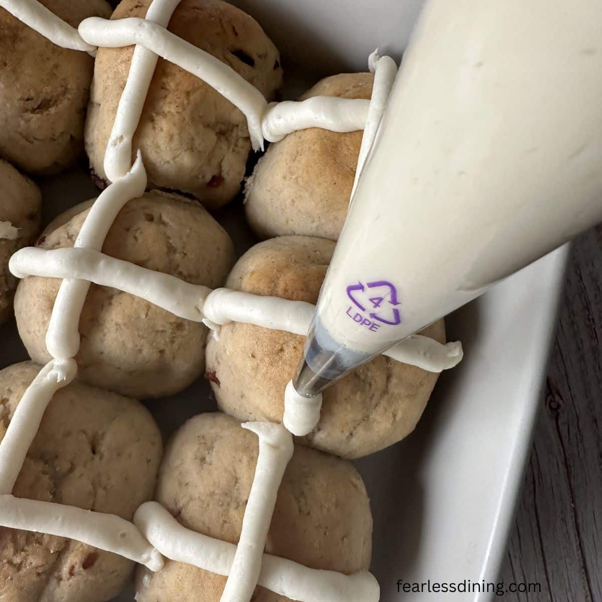 Piping the crosses with icing onto the rolls.