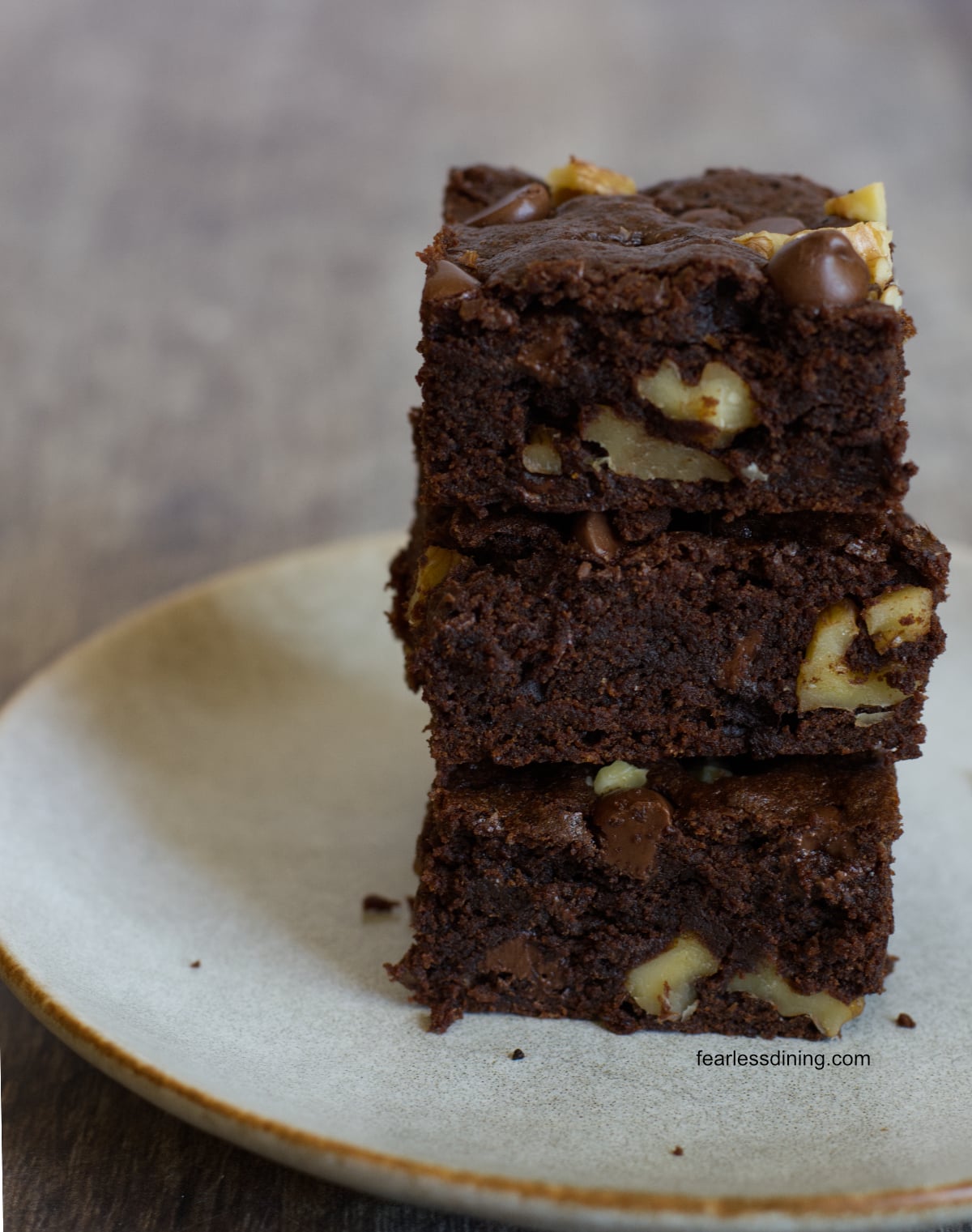 A stack of three gluten free chocolate walnut cookie bars on a plate.