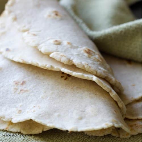 Flour tortillas on a kitchen towel folded over to show pliability.