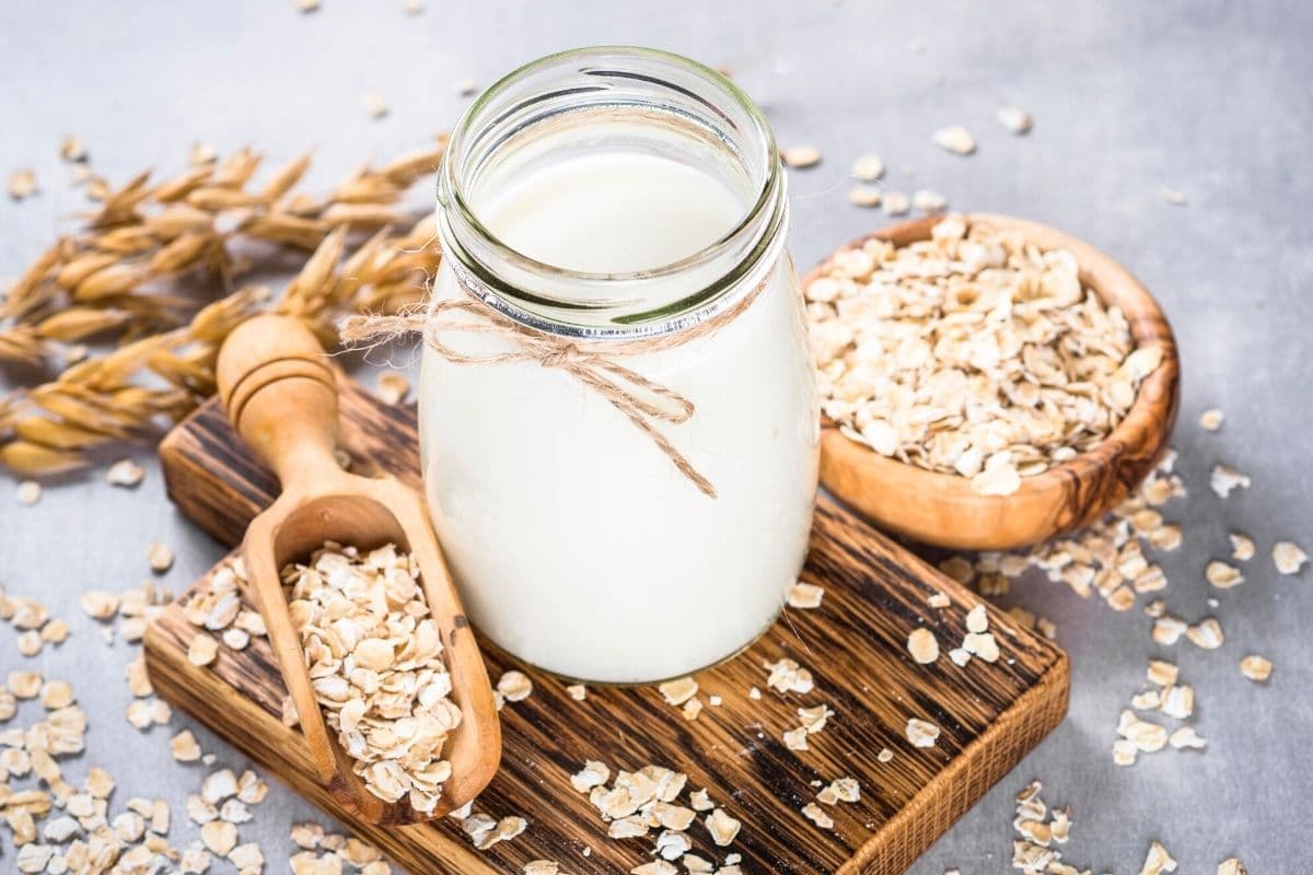 A jar of oat milk on a wooden board with oats.