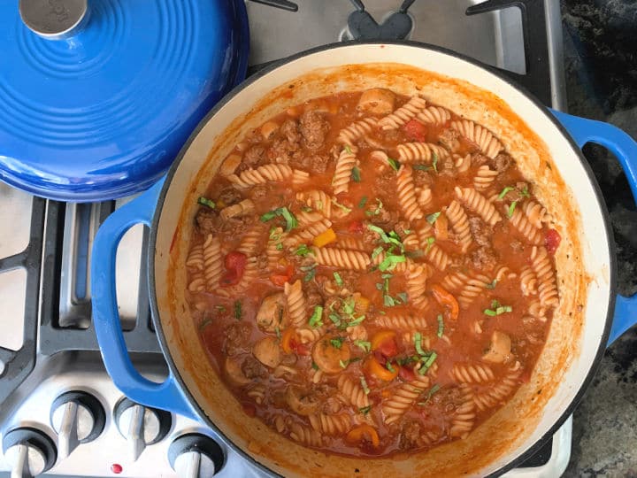 A photo of cooked pasta and sauce in a blue dutch oven.