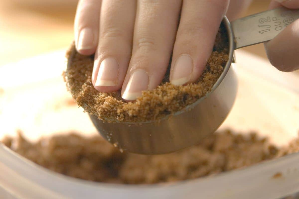 A hand packing brown sugar into a measuring scoop.