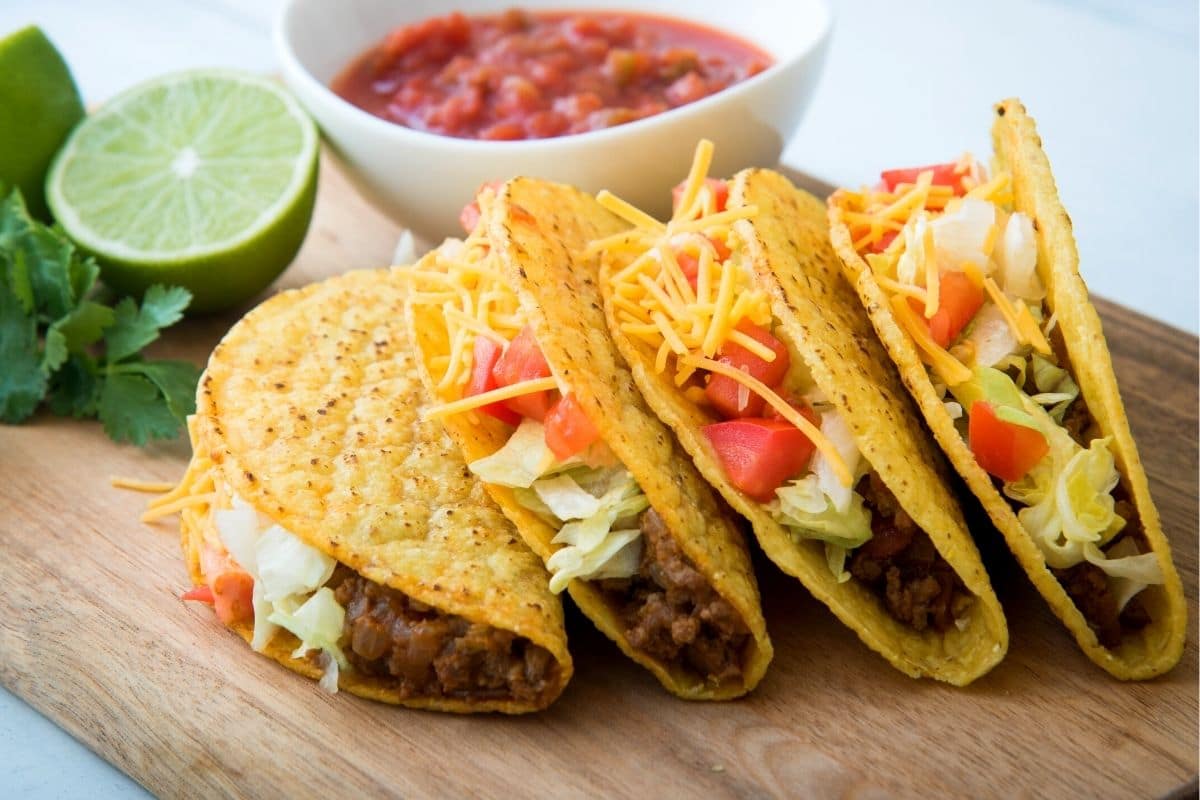 Four tacos on a wooden board.