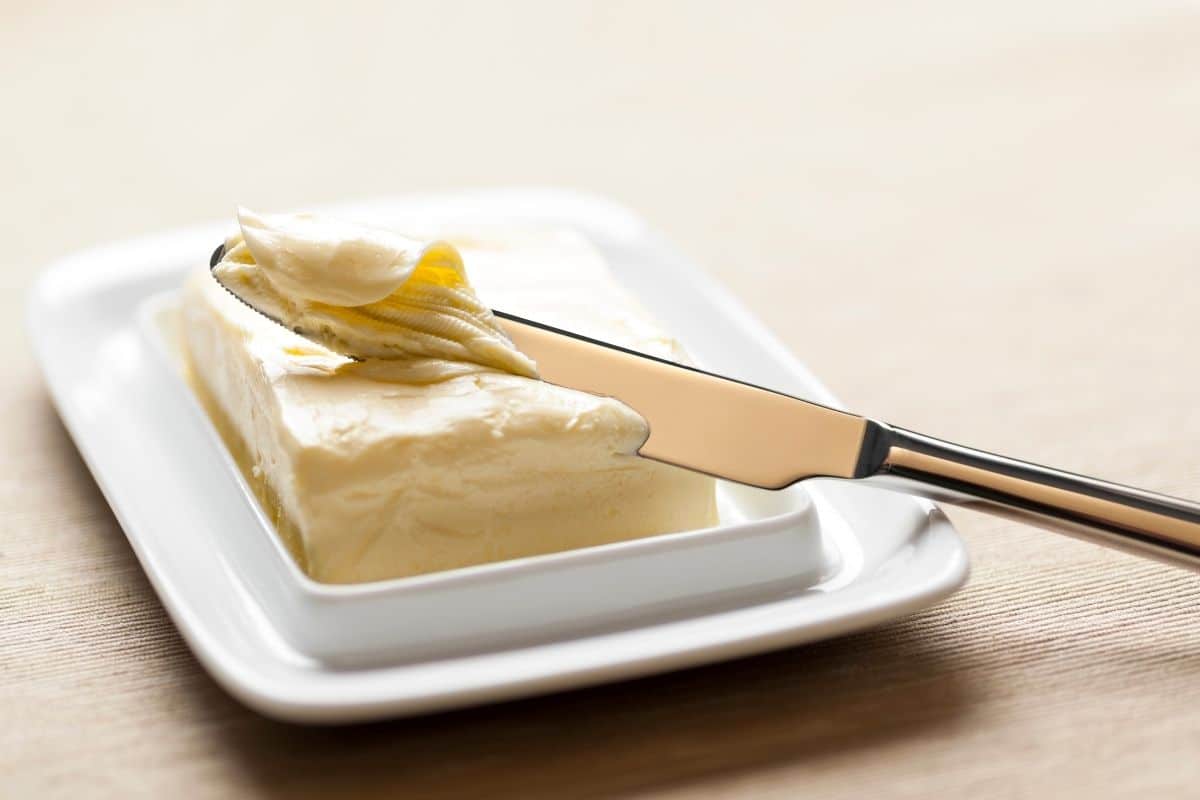 A knife scraping up margarine from the block.